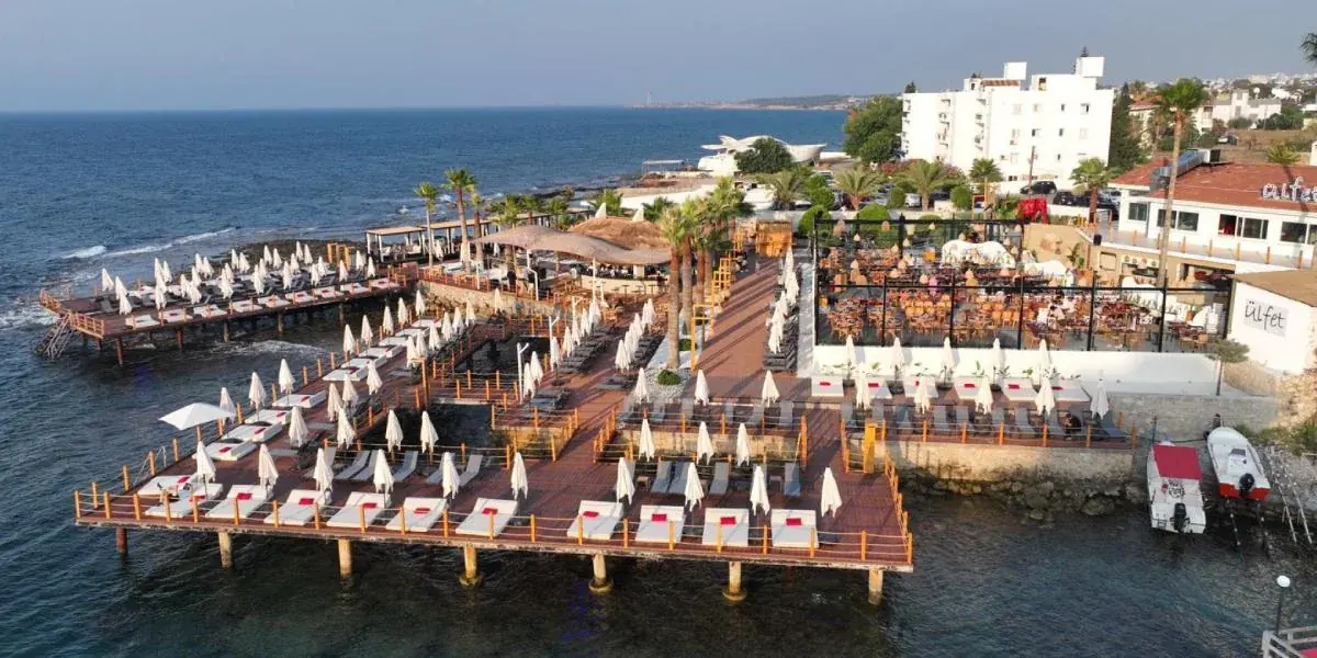 Girne Karaoğlanoğlu'ndaki Ülfet Beach Club'ın deniz üzerindeki iskeleleri, şezlongları ve restoranı.